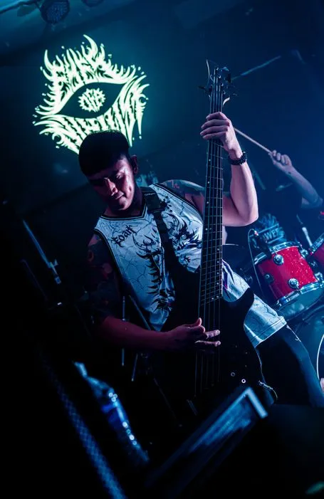 Eye of a Nihilist’s bassist under blue light beneath the band’s illuminated logo