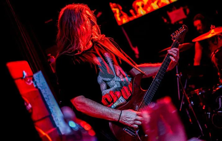 King Parrot’s guitarist with long red hair, playing under red light