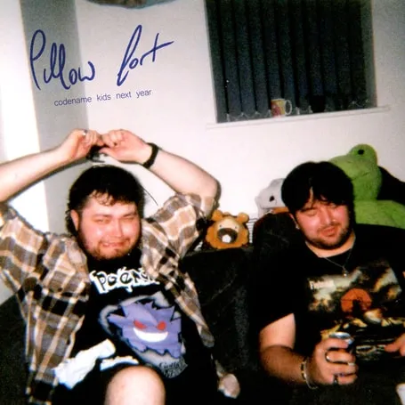 Single artwork for “Codename Kids Next Year”: two friends sitting on a bed surrounded by soft toys